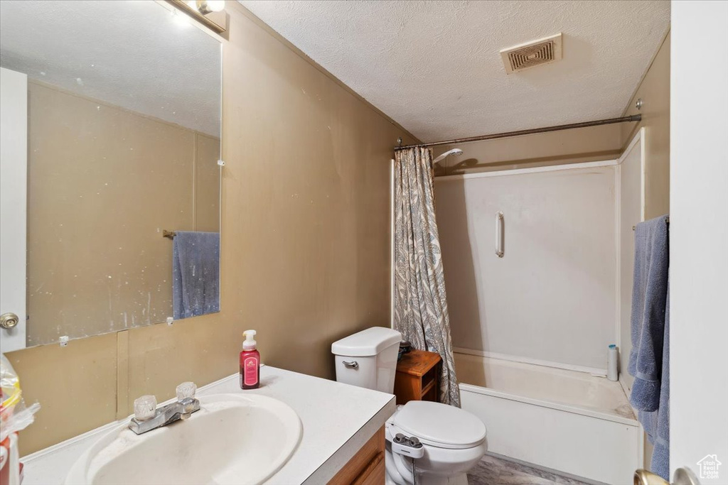 Full bathroom with vanity, toilet, shower / tub combo with curtain, and a textured ceiling