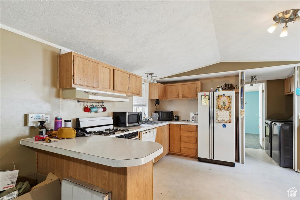 Kitchen featuring white appliances, a peninsula, under cabinet range hood, light countertops, and vaulted ceiling