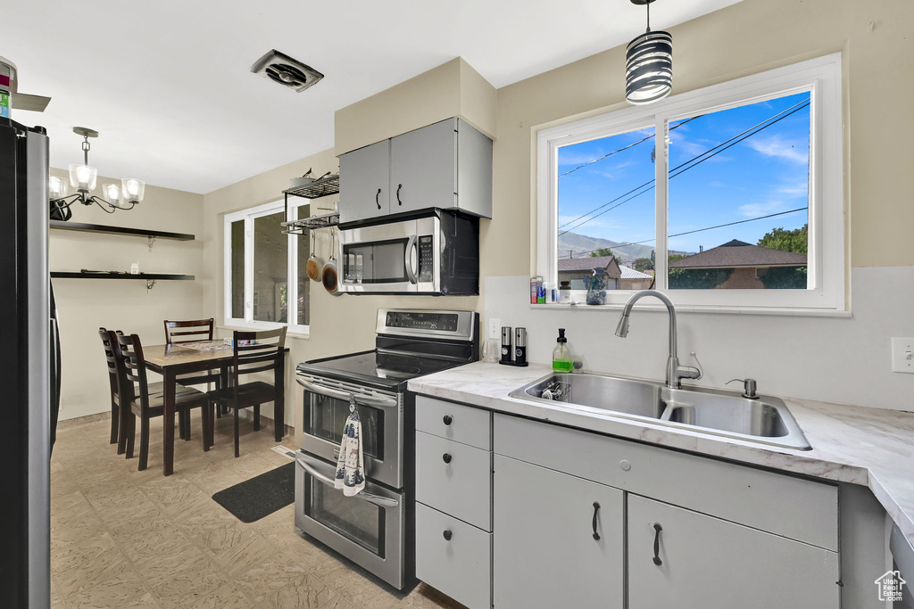 Kitchen with stainless steel appliances, light countertops, a chandelier, decorative light fixtures, and gray cabinetry