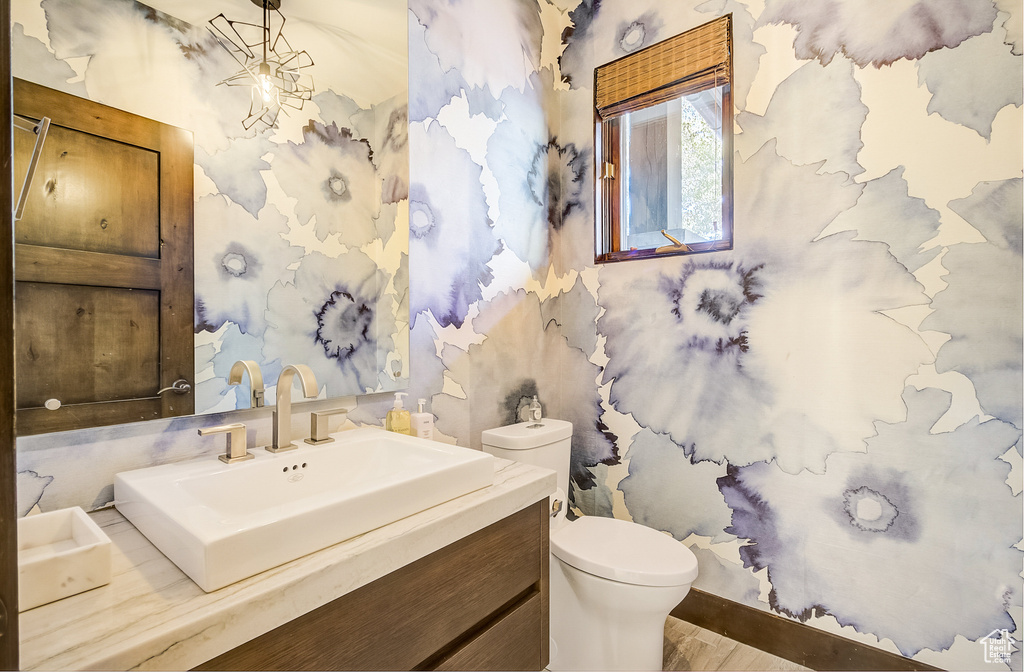 Bathroom with wallpapered walls, vanity, and wood finished floors