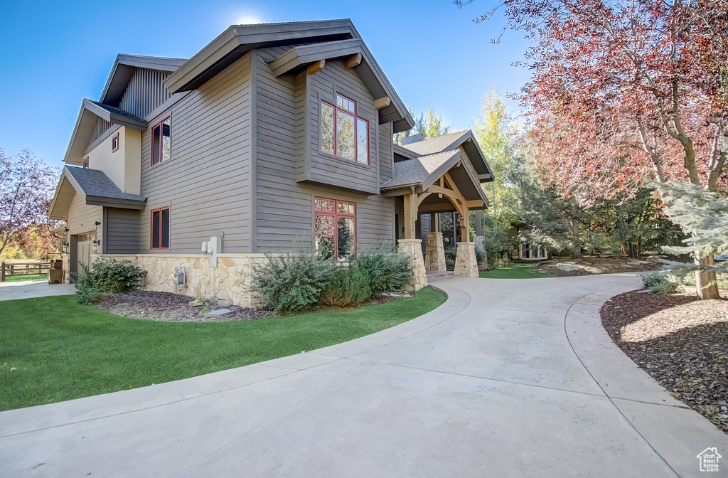 View of property exterior featuring stone siding, curved driveway, a yard, and a garage