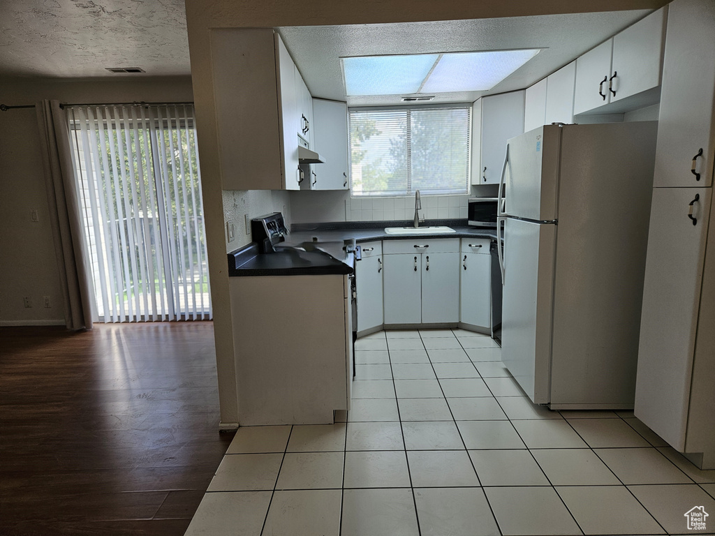 Kitchen with freestanding refrigerator, dark countertops, under cabinet range hood, white cabinetry, and stainless steel microwave