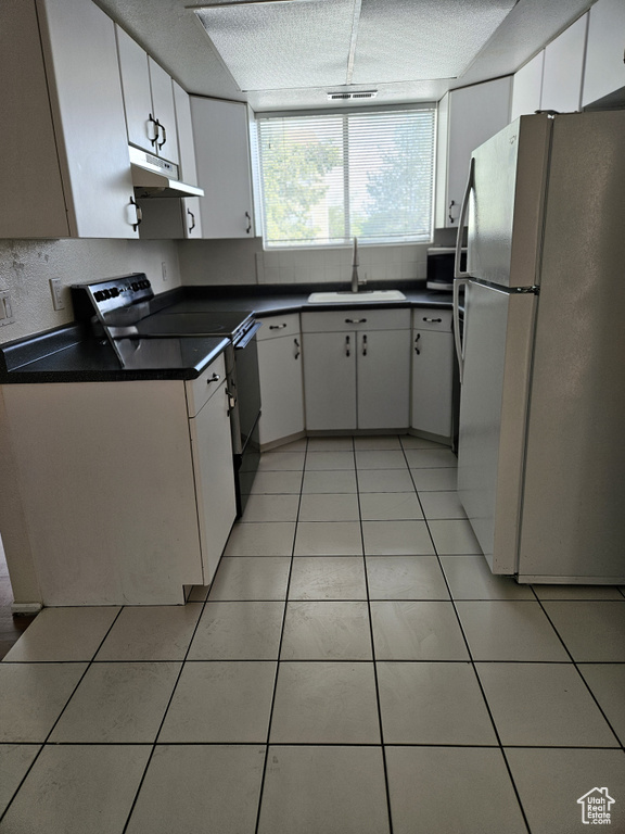 Kitchen with freestanding refrigerator, electric range, under cabinet range hood, dark countertops, and light tile patterned floors