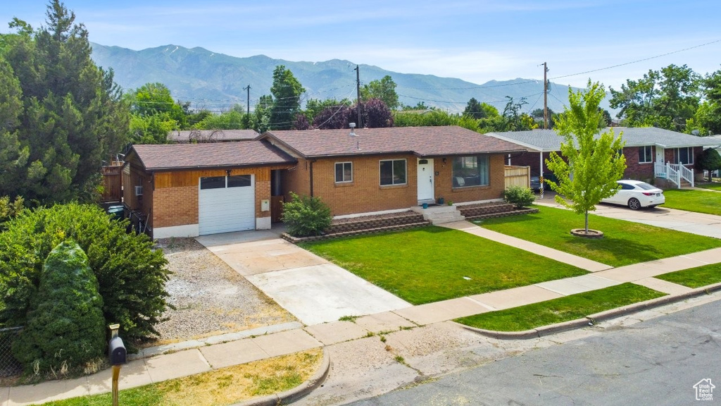 Ranch-style house featuring brick siding, an attached garage, driveway, a front lawn, and a mountain view