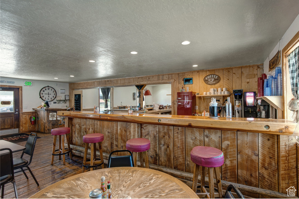 Indoor dry bar featuring hardwood / wood-style floors, a textured ceiling, wooden walls, recessed lighting, and plenty of natural light