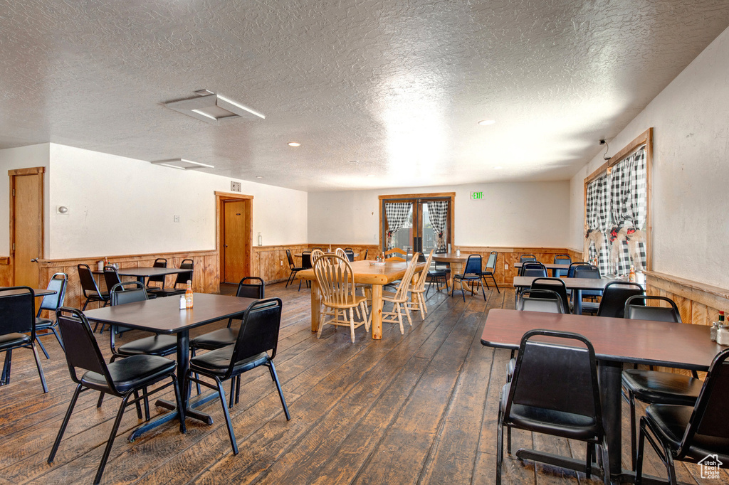 Dining room featuring a wainscoted wall, hardwood / wood-style flooring, a textured ceiling, and wooden walls