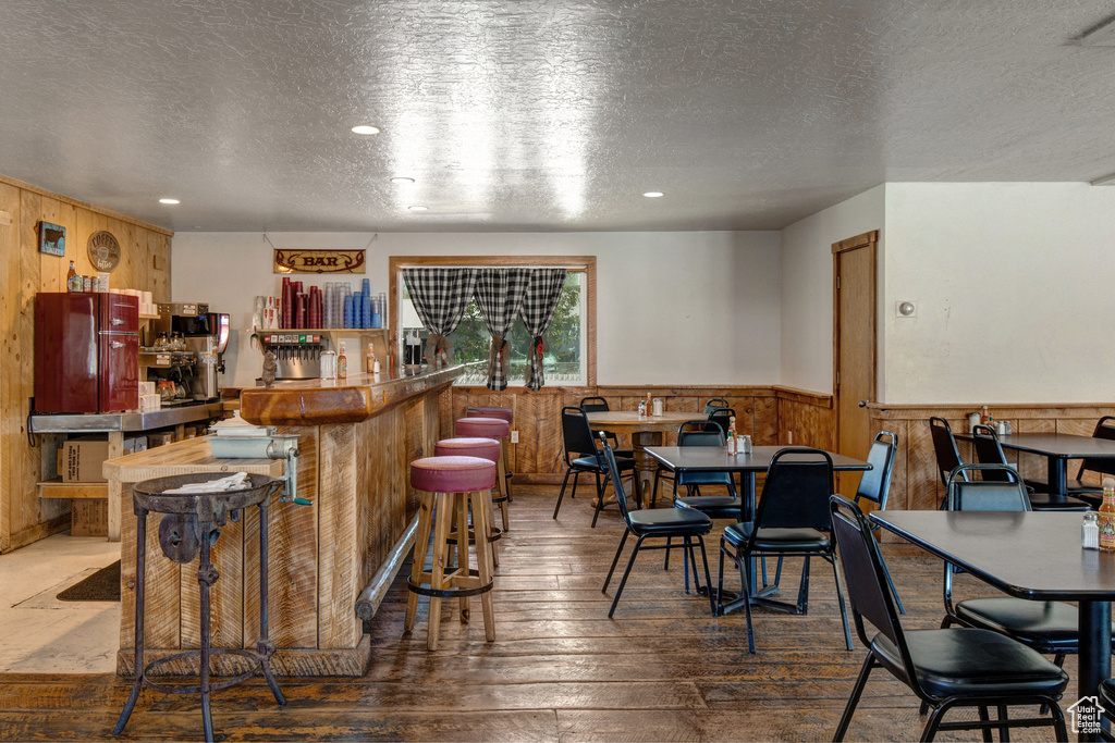 Community bar area featuring wooden walls, a textured ceiling, wainscoting, hardwood / wood-style floors, and recessed lighting