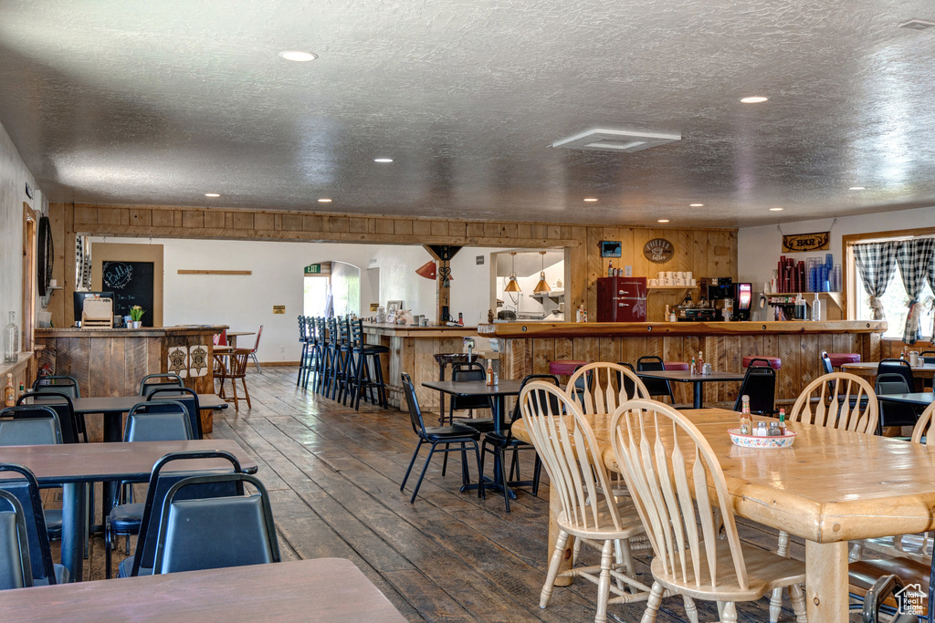 Dining space with wood-type flooring, a textured ceiling, recessed lighting, a bar, and wood walls