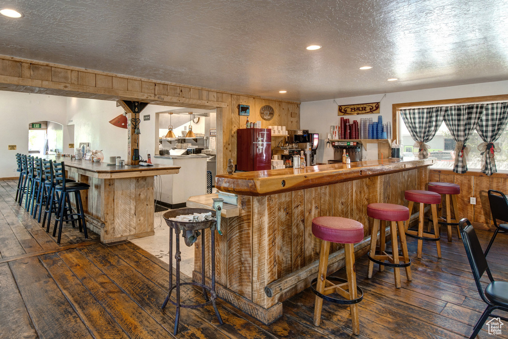 Community bar area with hardwood / wood-style floors, wooden walls, a textured ceiling, and recessed lighting