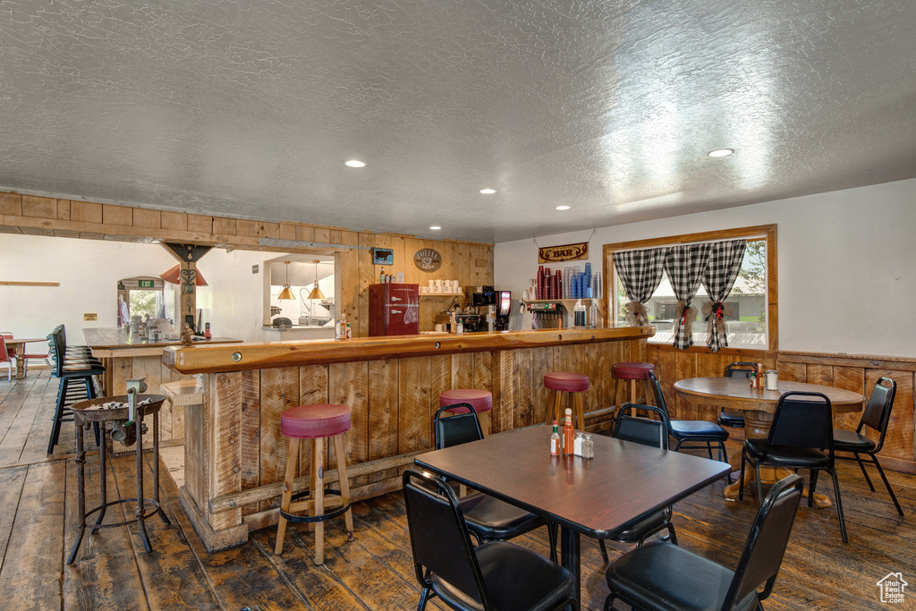 Dining area with hardwood / wood-style floors, wooden walls, recessed lighting, a textured ceiling, and wainscoting