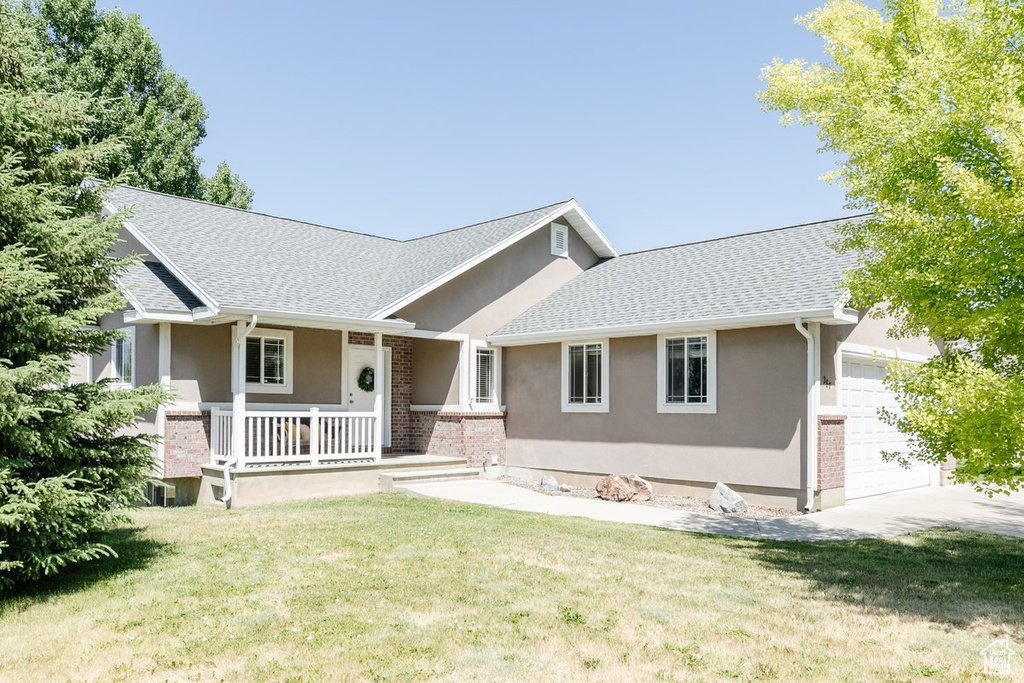 View of front of home featuring stucco siding, covered porch, a garage, and a front yard