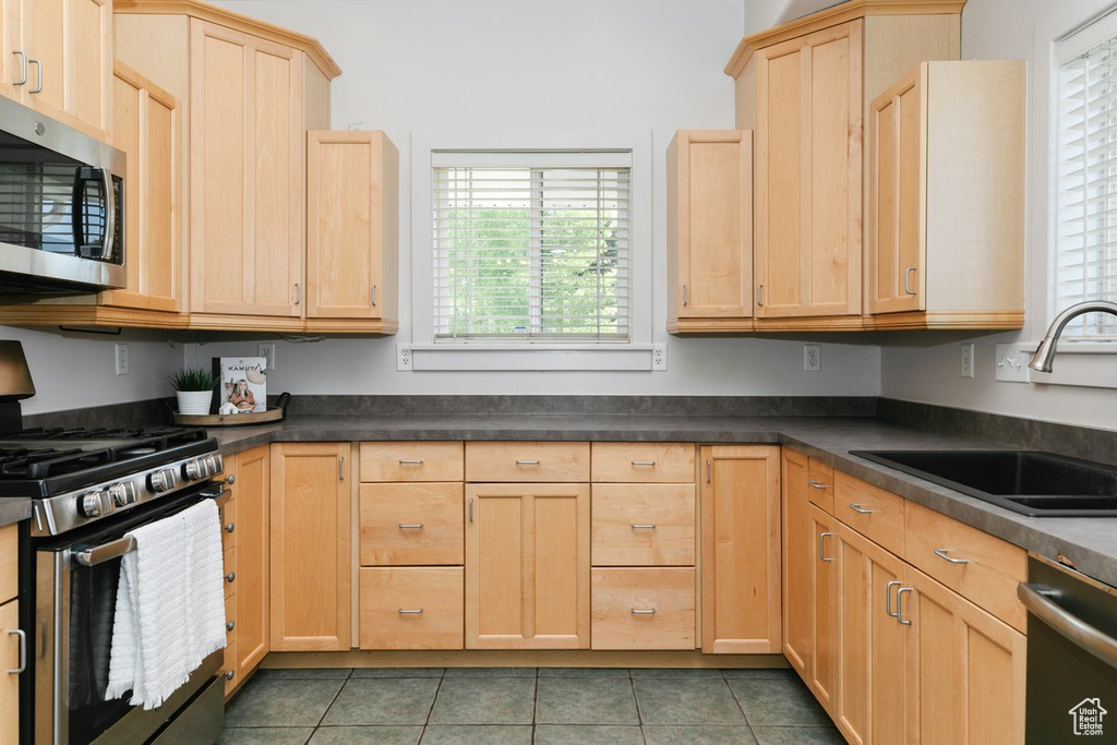 Kitchen featuring appliances with stainless steel finishes, light brown cabinetry, dark countertops, and tile patterned flooring