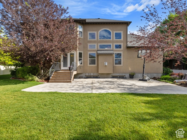 Rear view of house featuring stucco siding, a lawn, and a patio