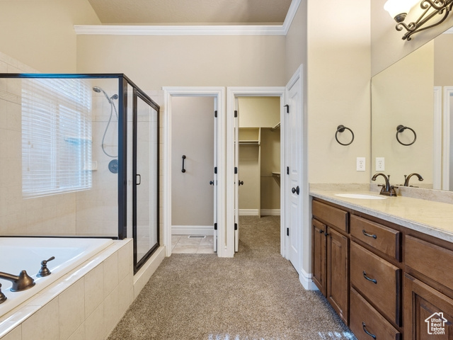 Bathroom featuring a stall shower, vanity, crown molding, a garden tub, and a walk in closet