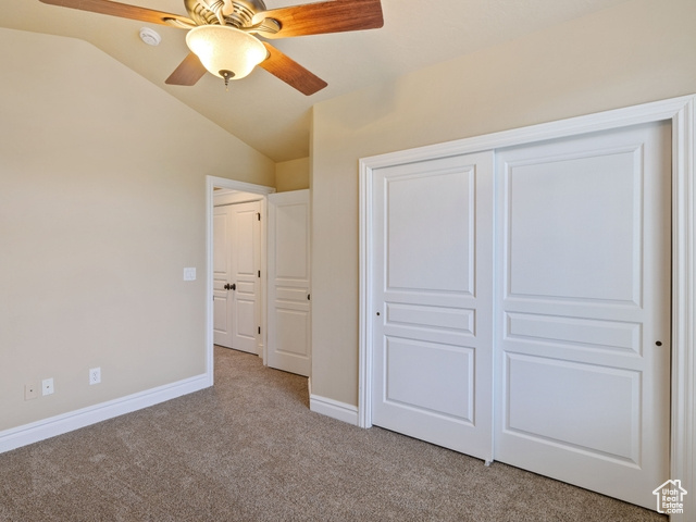 Unfurnished bedroom with carpet flooring, vaulted ceiling, a closet, and a ceiling fan