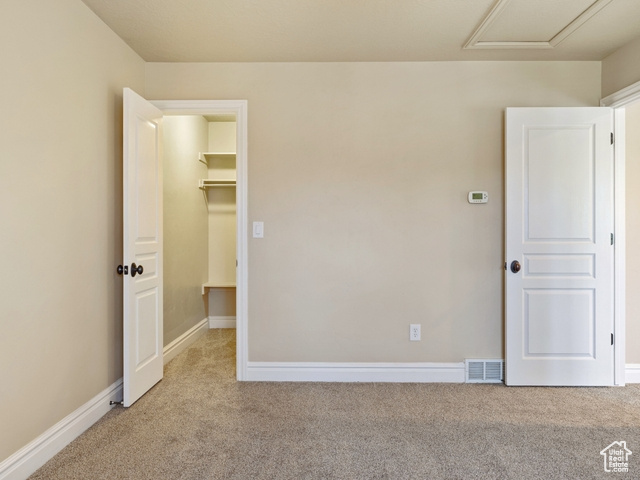 Unfurnished bedroom with carpet floors, a walk in closet, attic access, and a closet