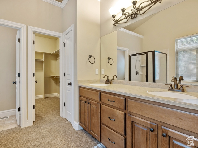 Bathroom featuring a shower stall, double vanity, ornamental molding, and a walk in closet