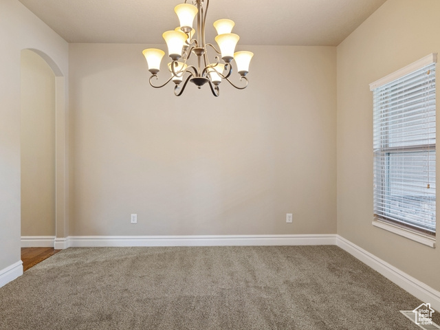 Carpeted spare room featuring a chandelier and arched walkways