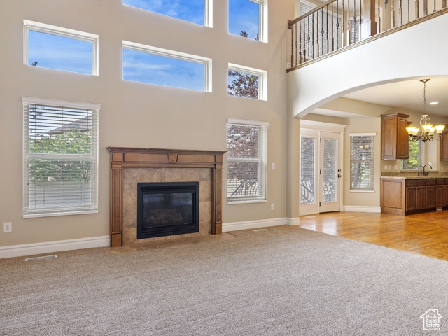 Unfurnished living room with light colored carpet, a chandelier, arched walkways, a towering ceiling, and a fireplace