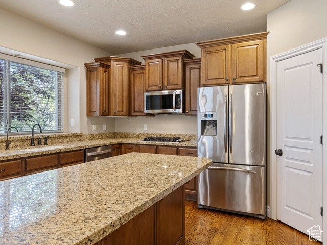 Kitchen featuring appliances with stainless steel finishes, brown cabinetry, light wood finished floors, light stone countertops, and recessed lighting