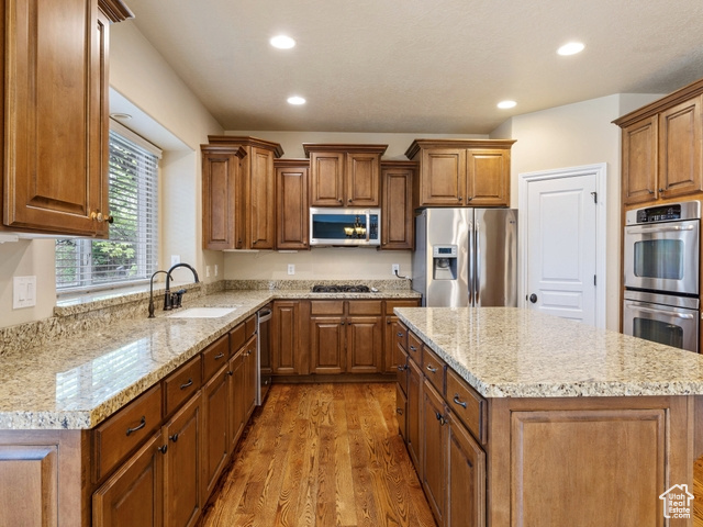 Kitchen with appliances with stainless steel finishes, light wood finished floors, brown cabinets, and recessed lighting