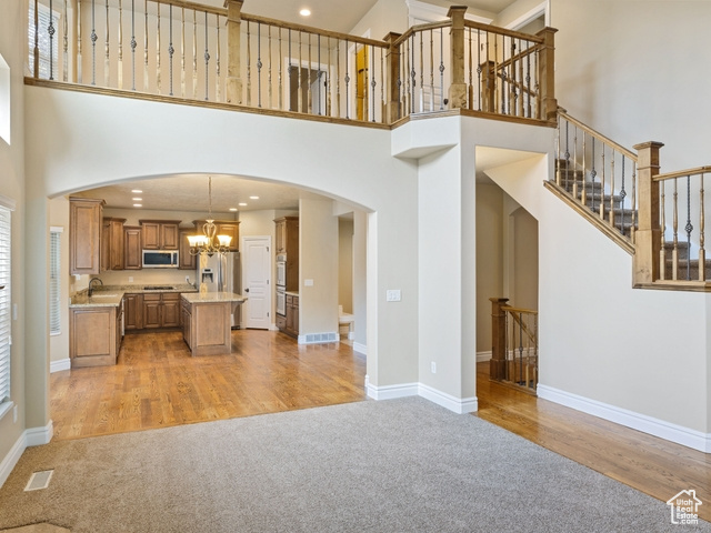 Unfurnished living room with light carpet, a high ceiling, a chandelier, arched walkways, and light wood-style flooring