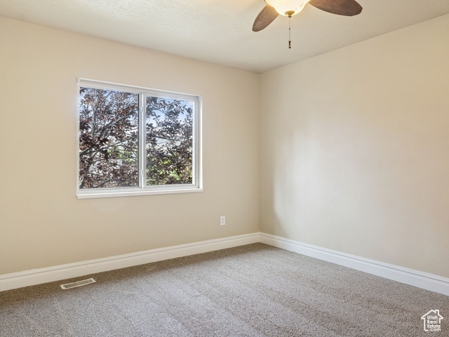 Carpeted spare room featuring a ceiling fan and baseboards
