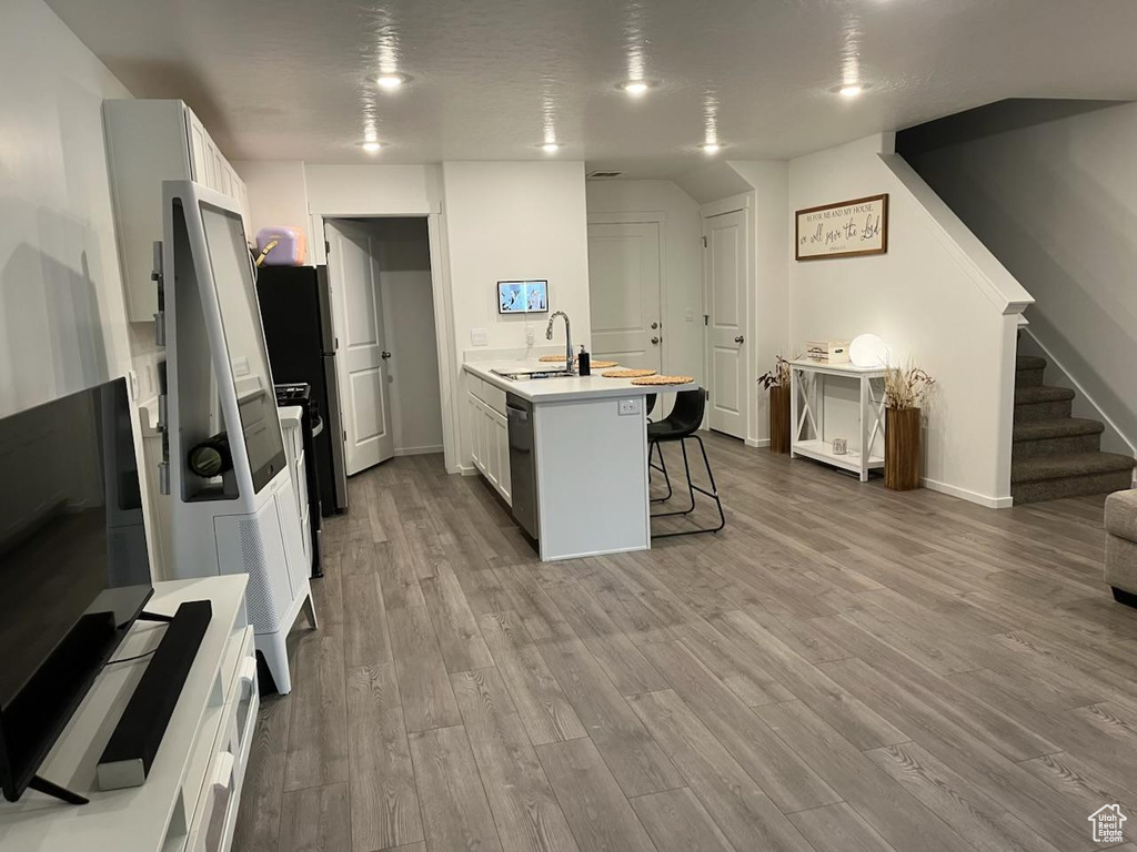 Kitchen featuring a kitchen bar, wood finished floors, light countertops, stainless steel dishwasher, and a peninsula
