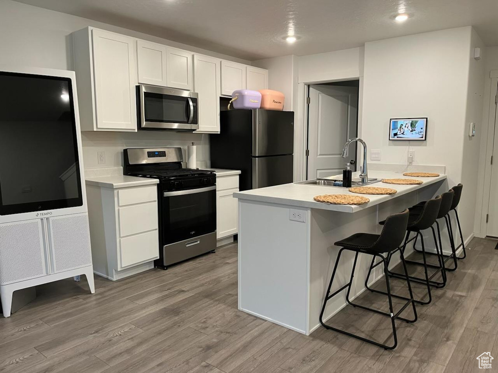 Kitchen featuring appliances with stainless steel finishes, wood finished floors, a kitchen bar, white cabinets, and recessed lighting