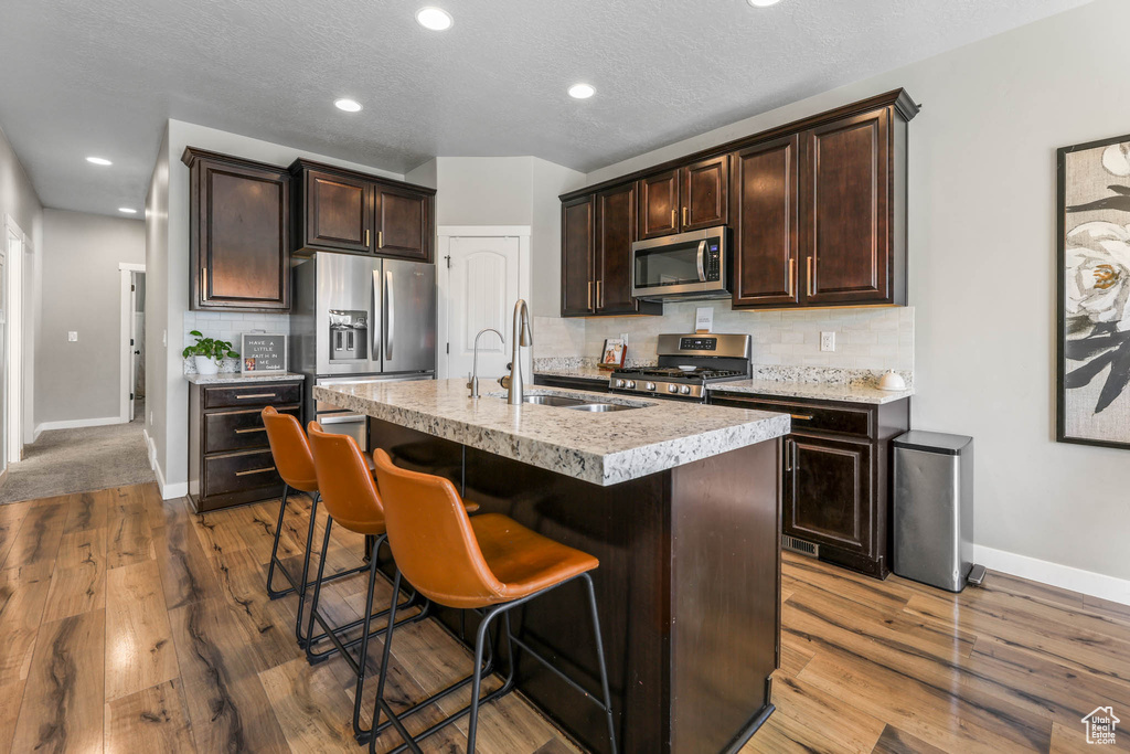 Kitchen with appliances with stainless steel finishes, dark brown cabinetry, tasteful backsplash, a breakfast bar, and recessed lighting