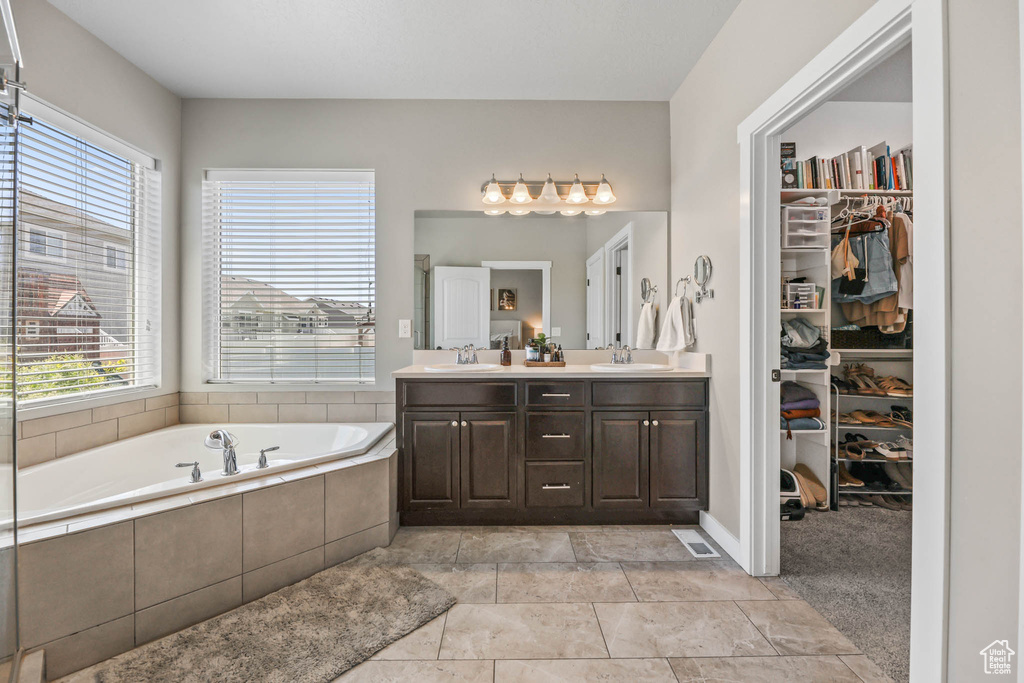 Bathroom with healthy amount of natural light, double vanity, a bath, and a spacious closet