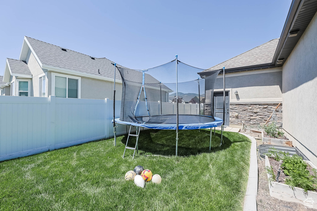 Fenced backyard featuring a trampoline and a garden