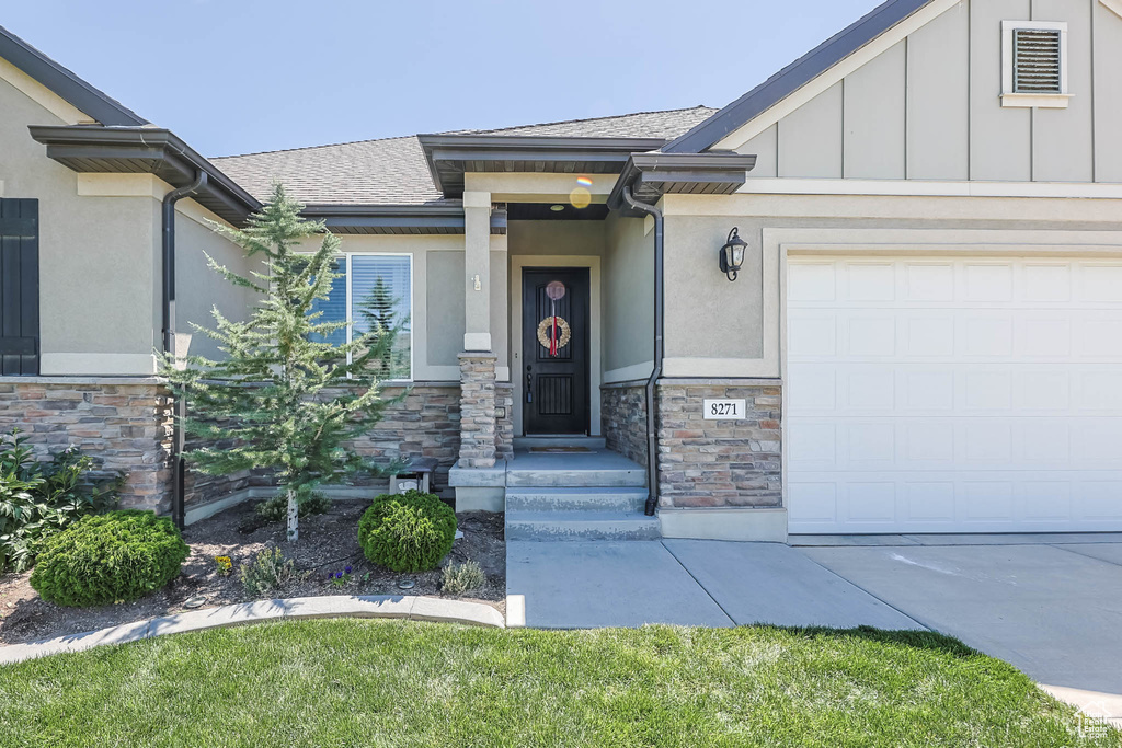 View of exterior entry featuring stone siding, stucco siding, an attached garage, roof with shingles, and board and batten siding