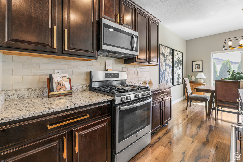 Kitchen featuring appliances with stainless steel finishes, backsplash, light wood finished floors, and light stone counters
