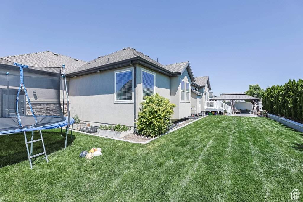 View of side of property with a trampoline, a gazebo, stucco siding, and a lawn
