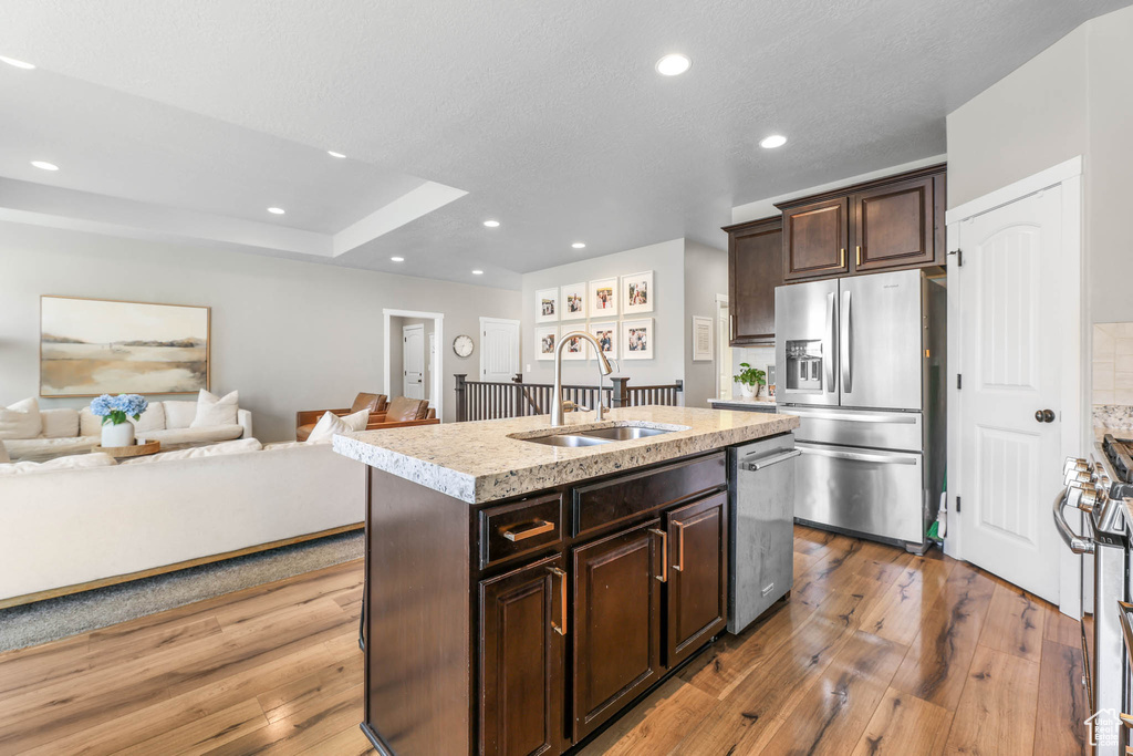 Kitchen with appliances with stainless steel finishes, light countertops, hardwood / wood-style floors, dark brown cabinets, and a center island with sink