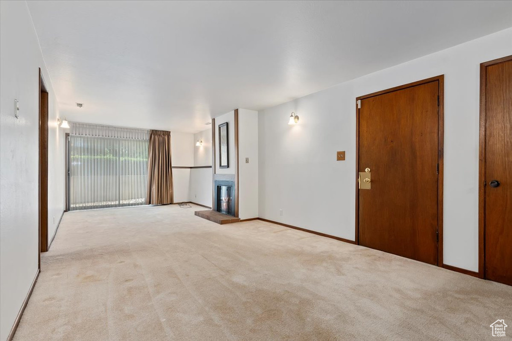 Unfurnished room featuring light carpet and a fireplace with raised hearth
