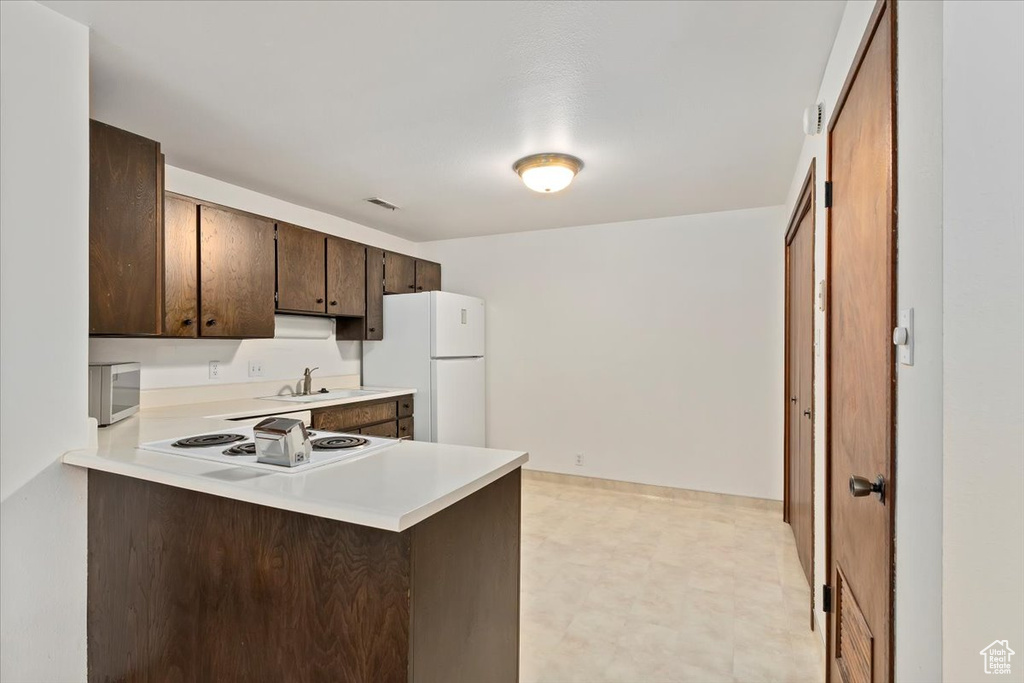 Kitchen featuring white appliances, light countertops, light flooring, dark brown cabinets, and a peninsula