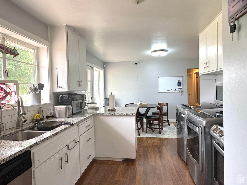 Kitchen with dishwasher, a peninsula, dark wood-type flooring, and white cabinetry