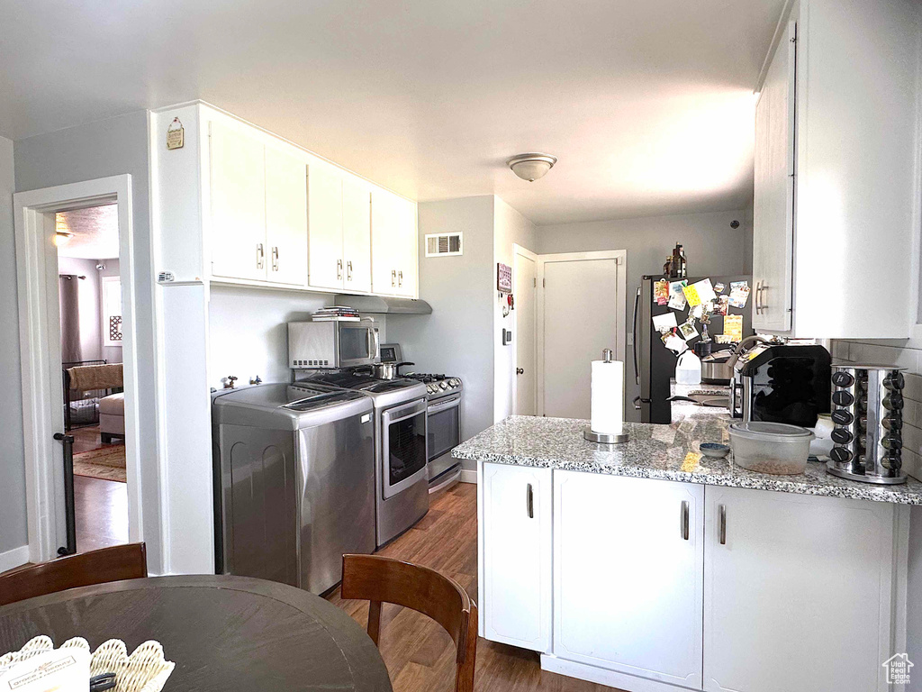 Kitchen with stainless steel appliances, a peninsula, wood finished floors, white cabinets, and light stone counters