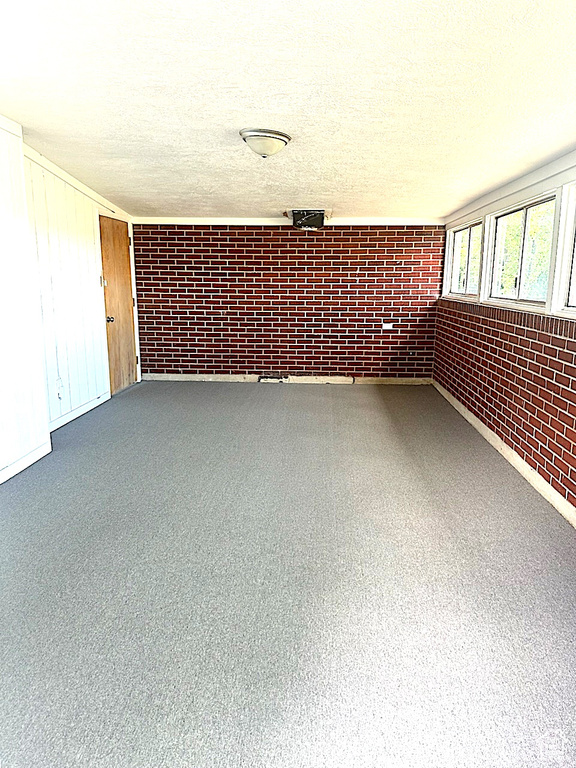 Empty room featuring brick wall and a textured ceiling
