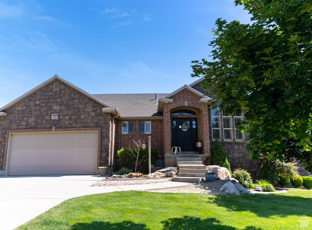 View of front facade with a front yard, driveway, an attached garage, and brick siding