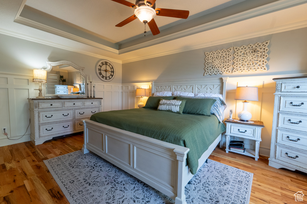 Bedroom with a decorative wall, a raised ceiling, wood finished floors, crown molding, and wainscoting