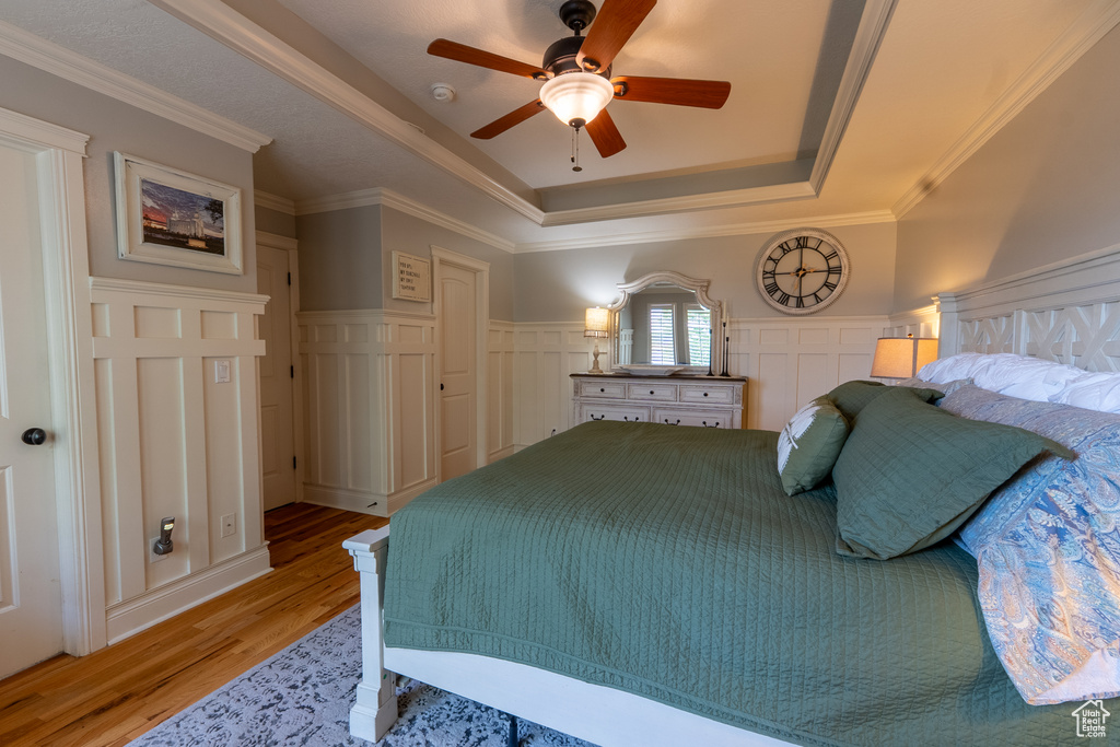 Bedroom featuring a raised ceiling, light wood-type flooring, a decorative wall, wainscoting, and crown molding