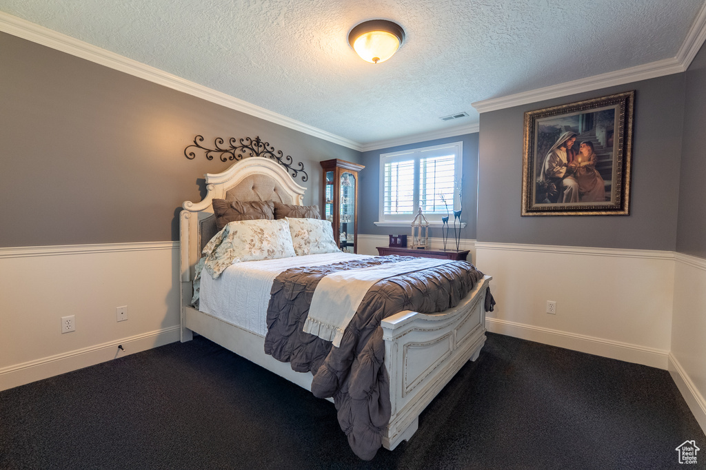 Bedroom with a textured ceiling, ornamental molding, and dark colored carpet
