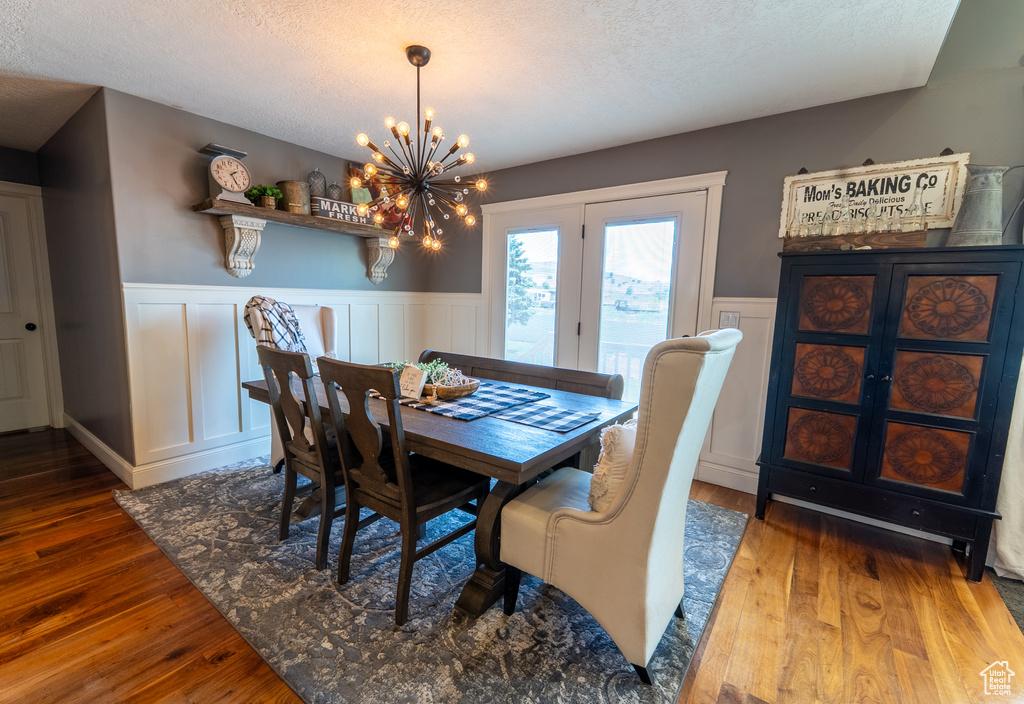 Dining room featuring a wainscoted wall, a chandelier, wood-type flooring, a textured ceiling, and a decorative wall