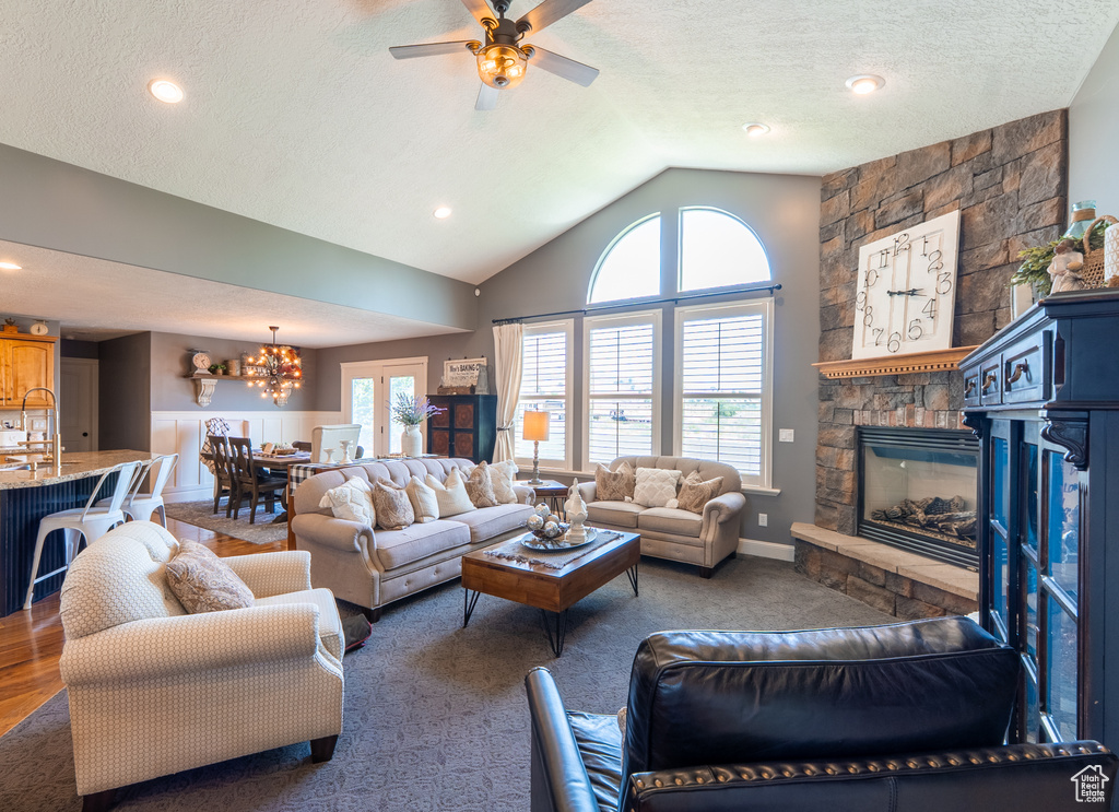 Living room featuring lofted ceiling, ceiling fan, a chandelier, a stone fireplace, and a textured ceiling