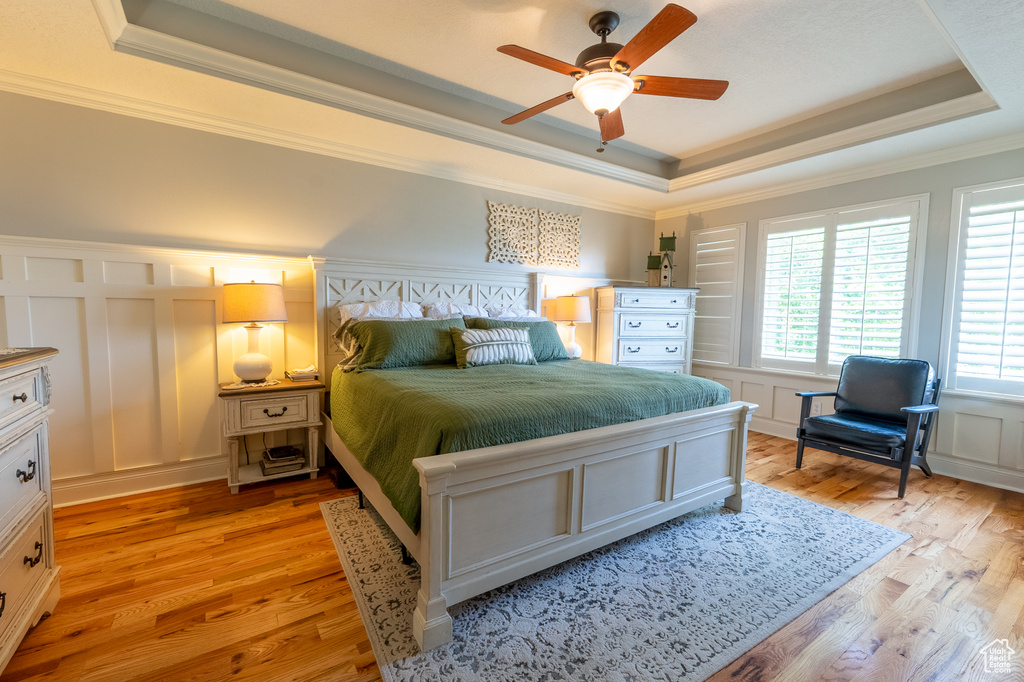 Bedroom with a raised ceiling, a decorative wall, light wood-style flooring, ornamental molding, and a ceiling fan