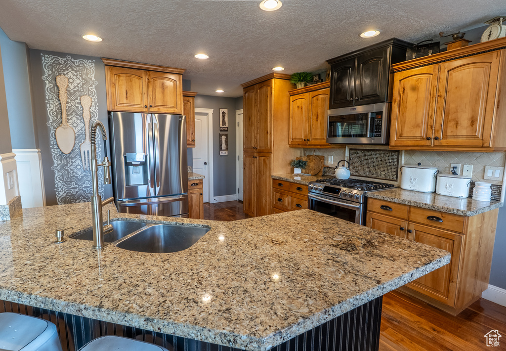 Kitchen featuring appliances with stainless steel finishes, dark wood-type flooring, light stone counters, a kitchen bar, and a peninsula