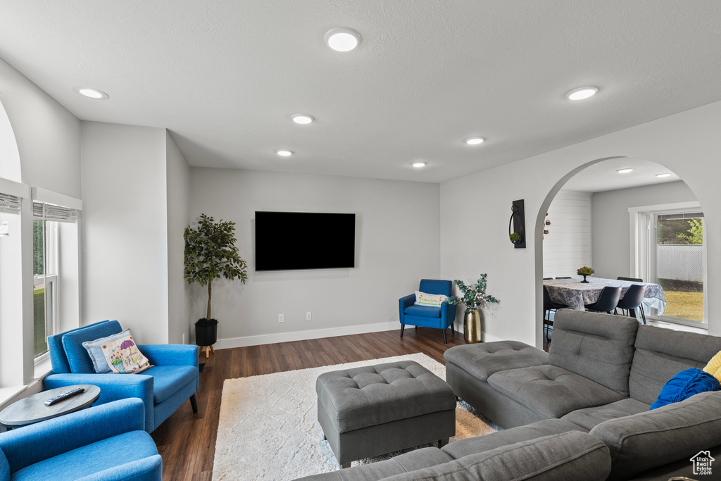 Living room with arched walkways, dark wood-style floors, and recessed lighting